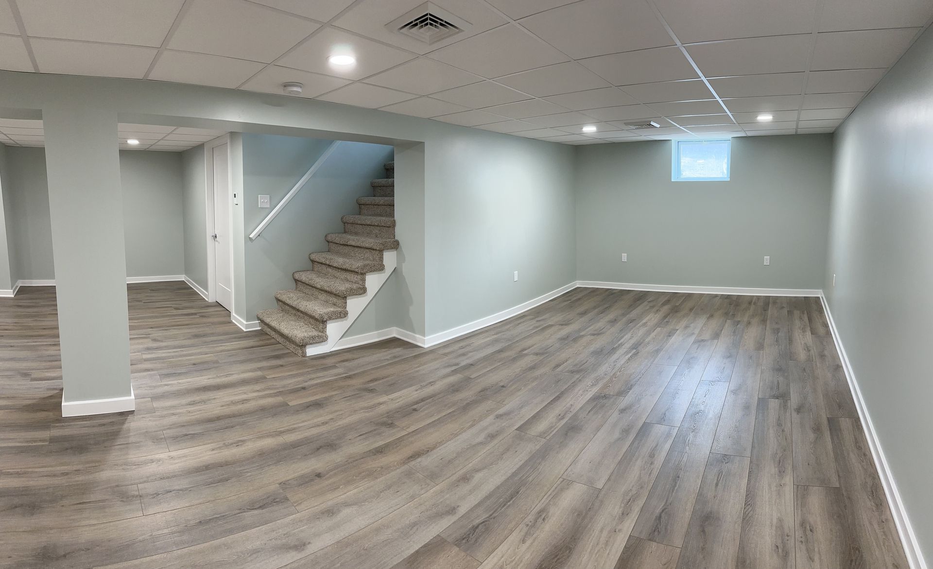 Empty finished basement with gray wood-look flooring, light blue walls, stairs, and recessed lighting.