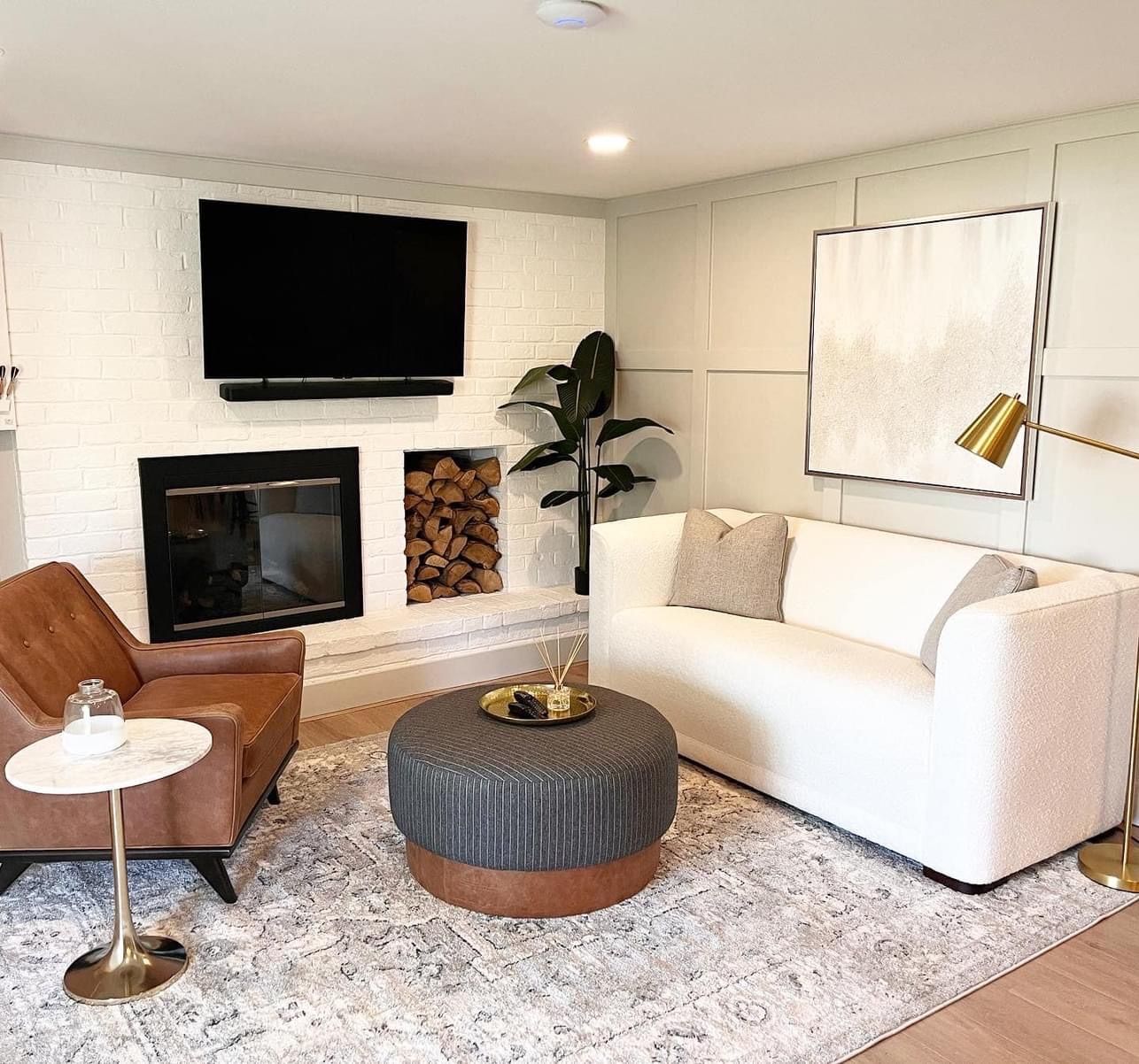 Cozy living room with fireplace, white brick, sofa, chair, ottoman, and abstract art.