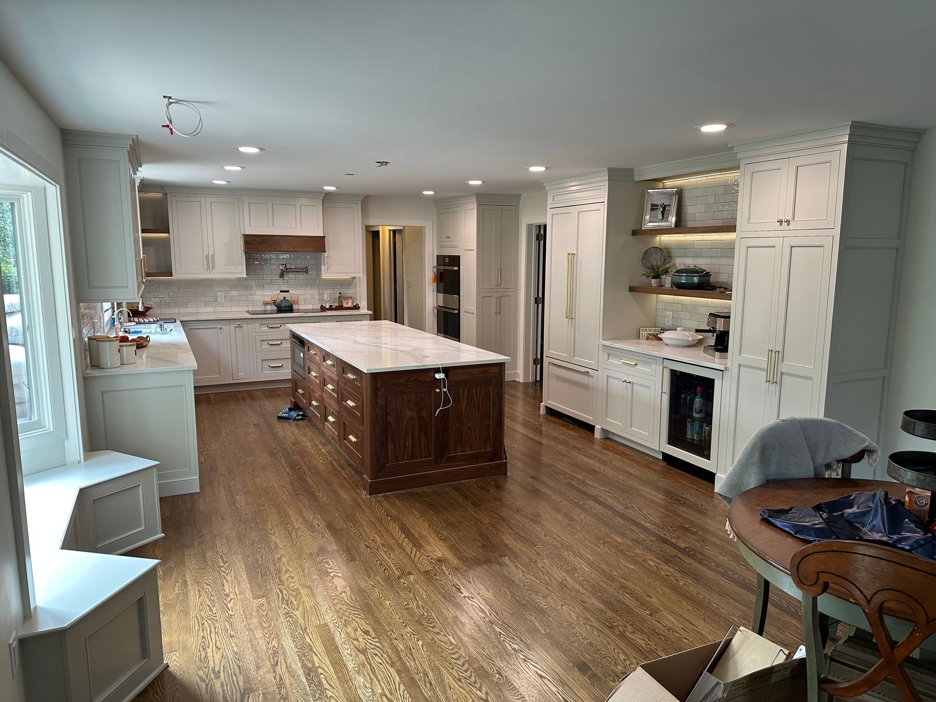 Spacious white kitchen with dark wood island, cabinets, and hardwood floors. Features include a beverage cooler, shelving, and large window.