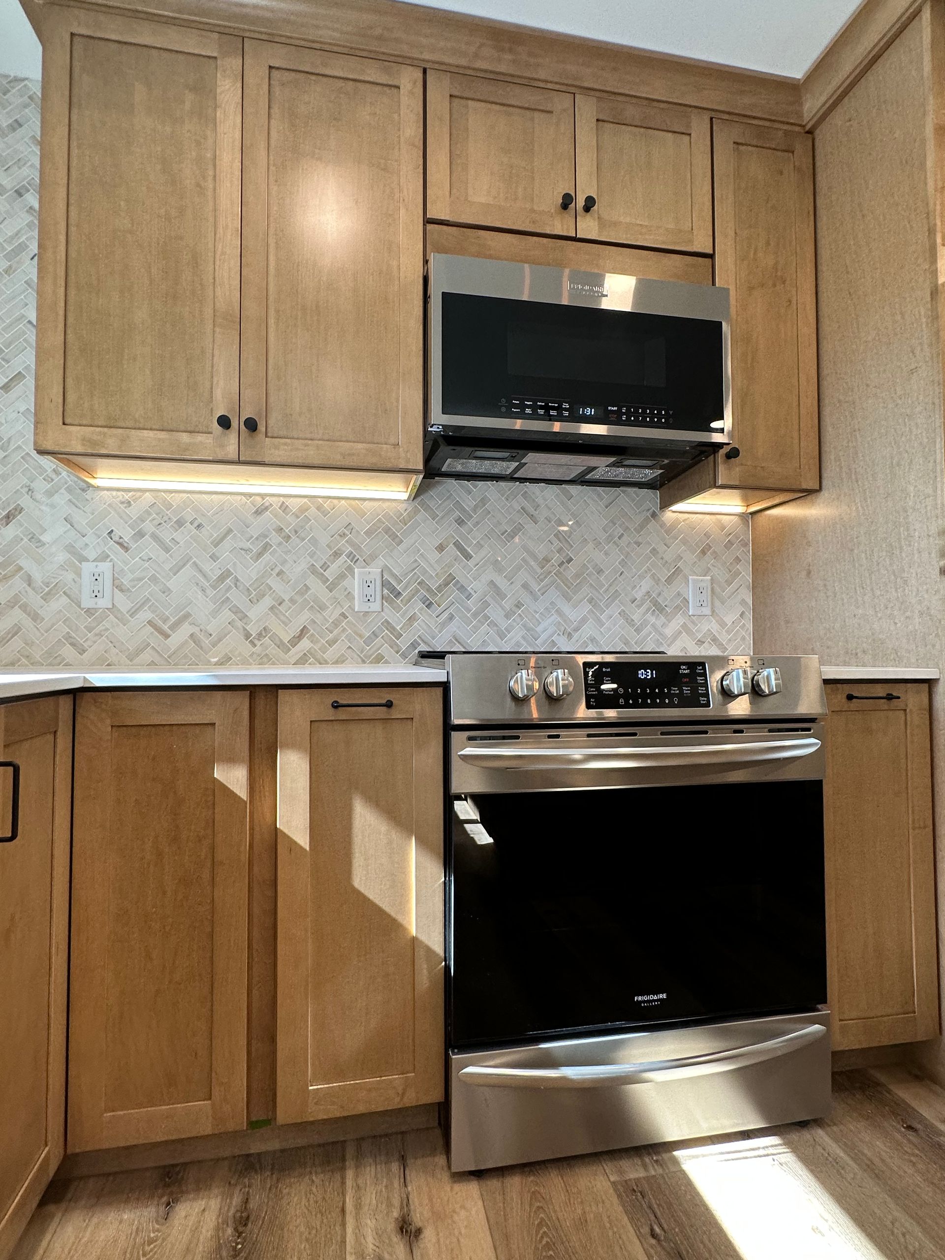 Kitchen with light wood cabinets, stainless steel appliances, and white tiled backsplash.
