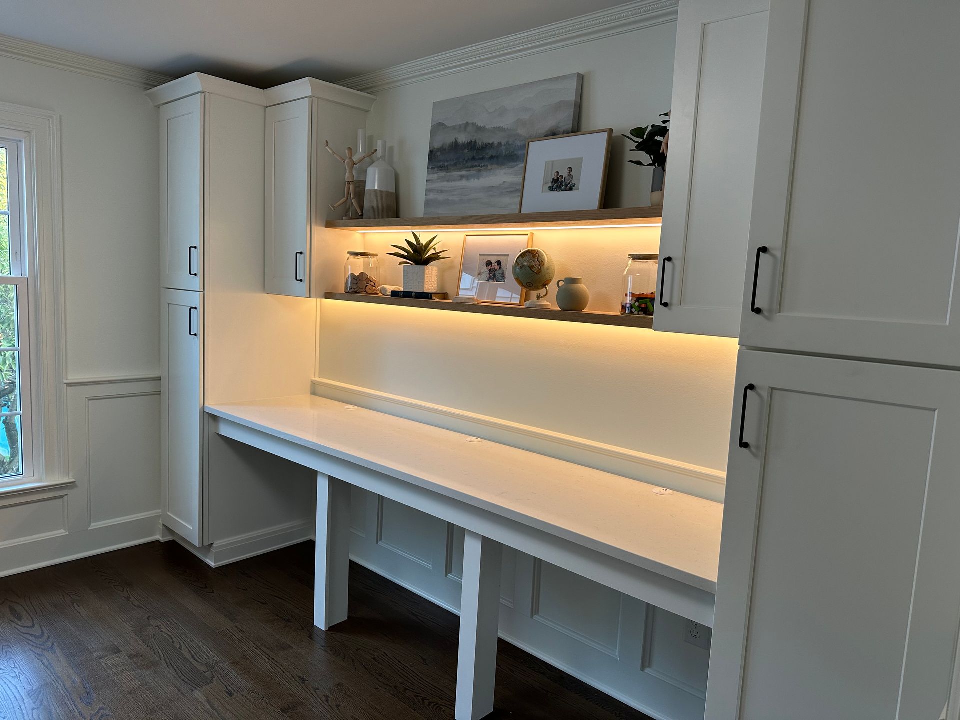 Built-in white desk with overhead shelf lit by LED strip, flanked by white storage cabinets.