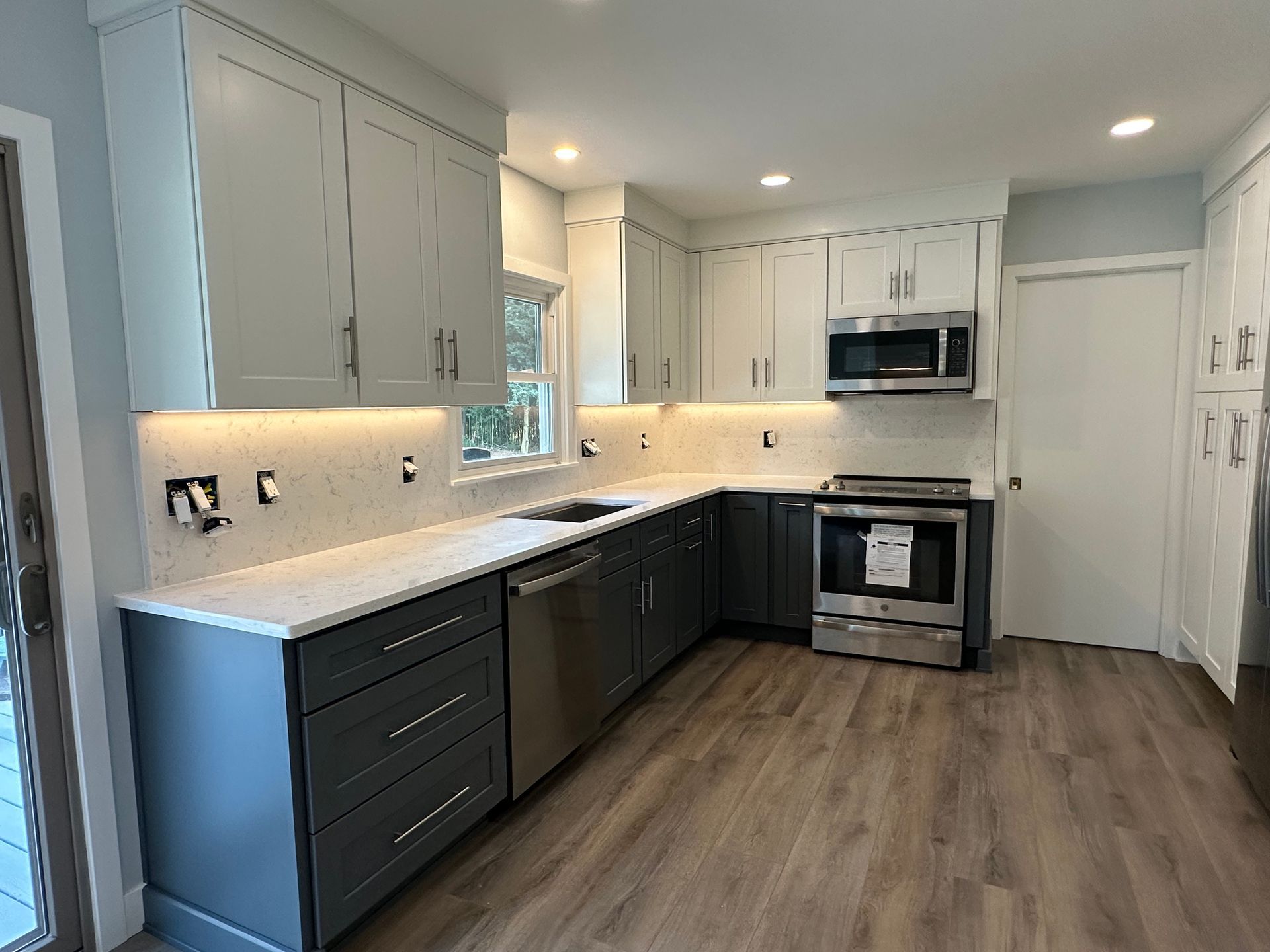 Modern kitchen with gray and white cabinets, stainless steel appliances, and wood-look flooring.