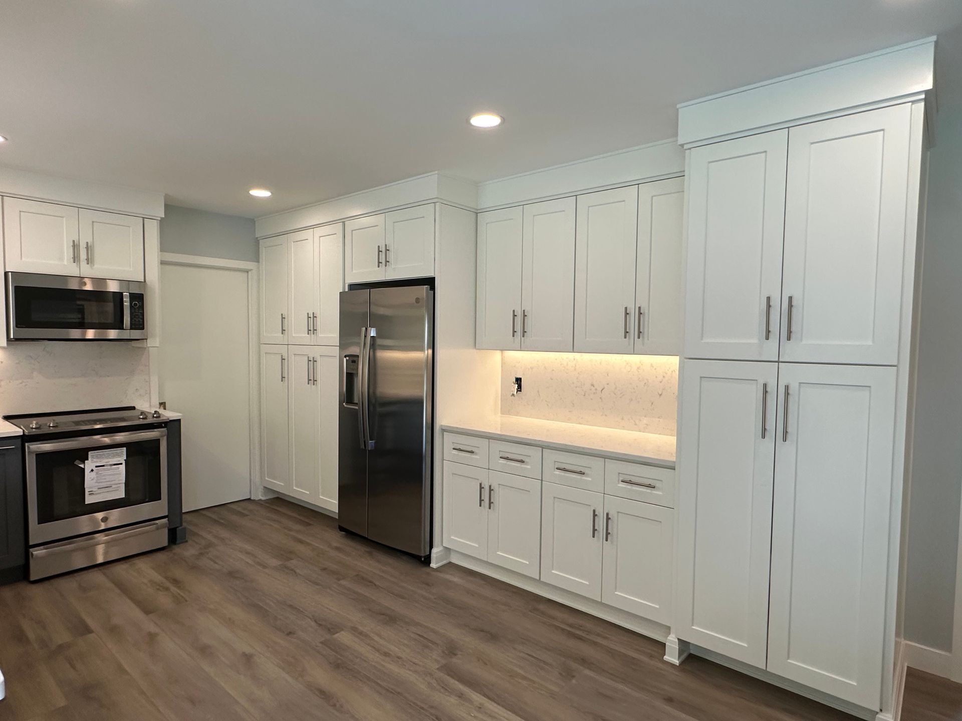 White kitchen with cabinets, stainless steel appliances, and wood-look flooring.