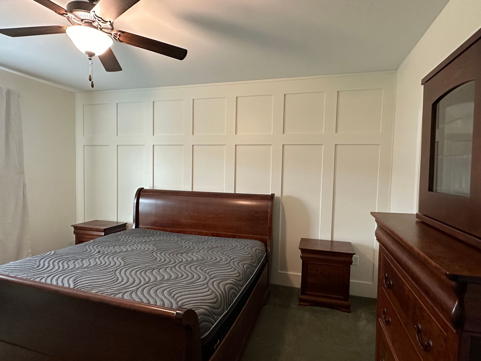 Bedroom with dark wood bed, nightstands, dresser, and paneling on wall.
