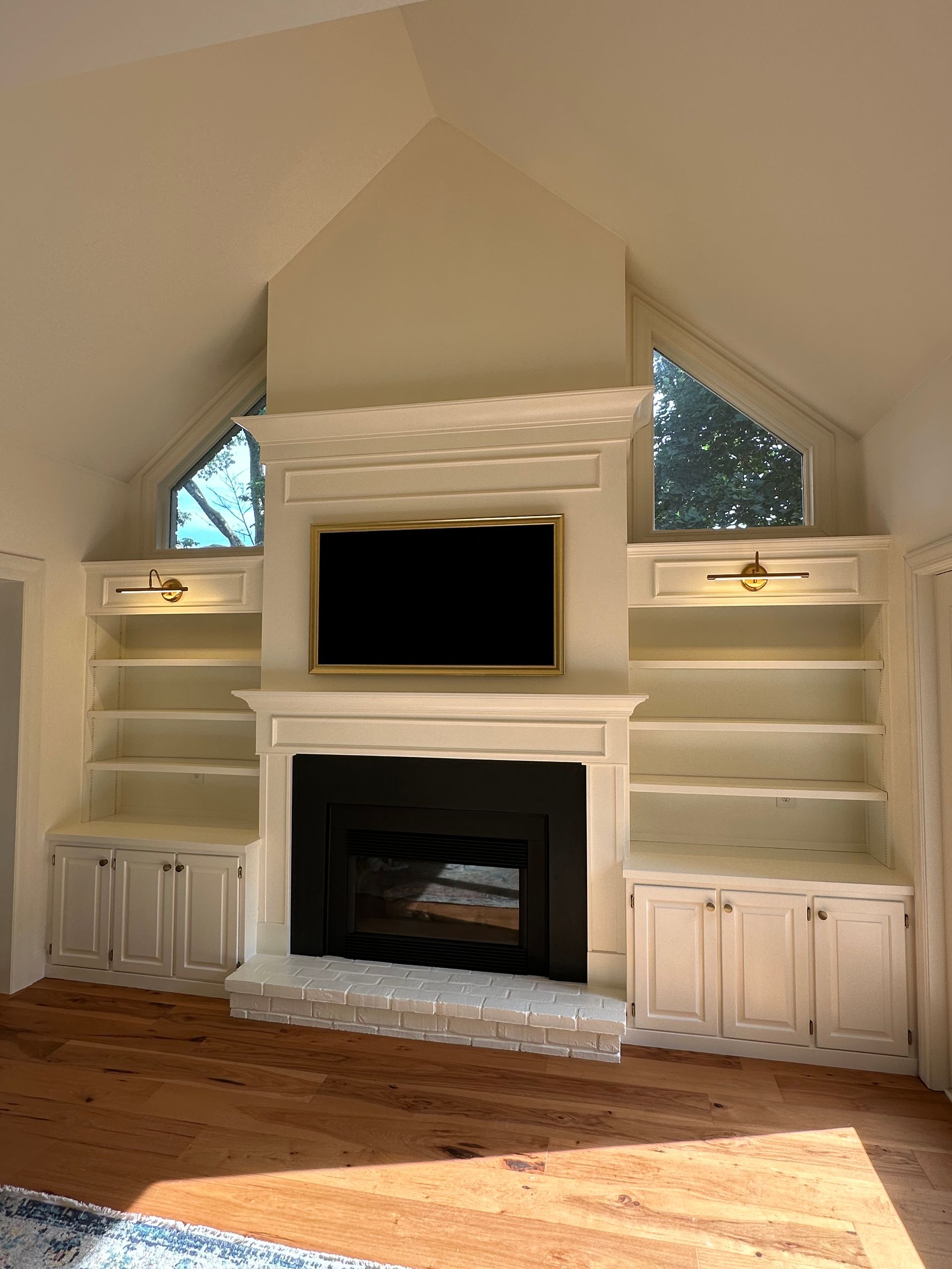Fireplace with built-in bookshelves and TV centered in a light-colored room with two triangular windows.