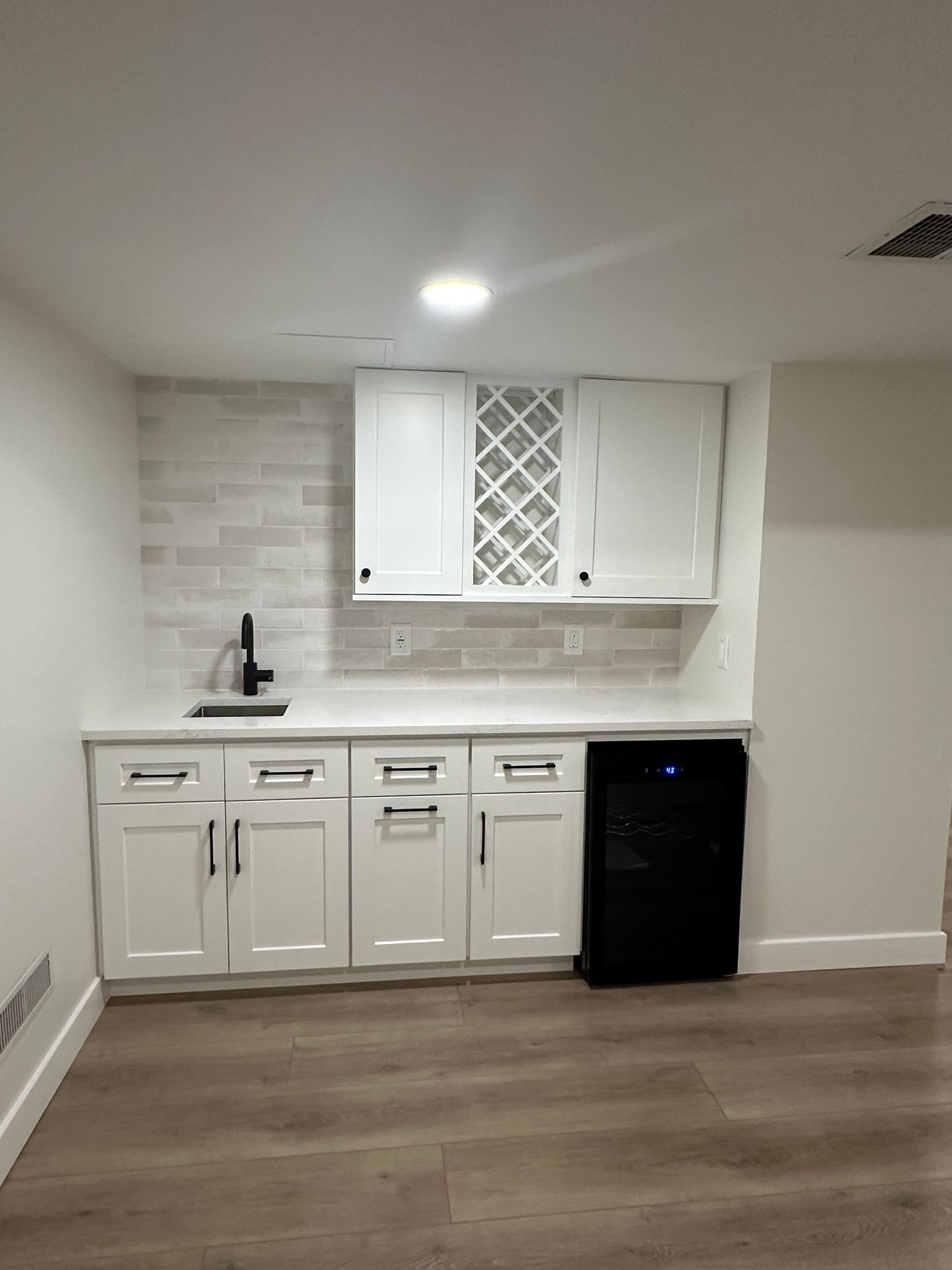 White kitchen cabinets with black handles and faucet; a wine rack is installed between two upper cabinets.