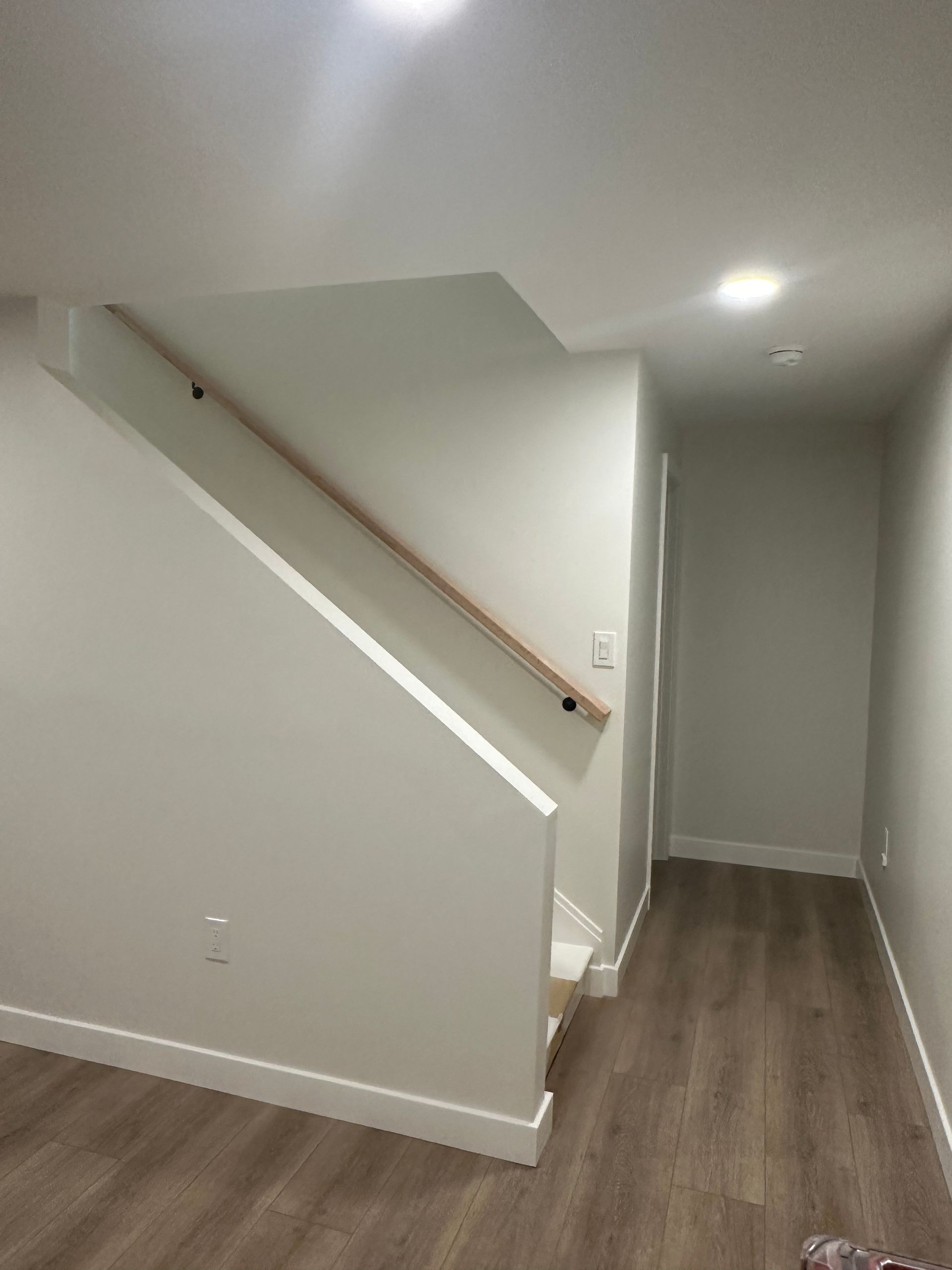 Interior view of stairs and hallway, white walls, wood handrail, and wood-look flooring.