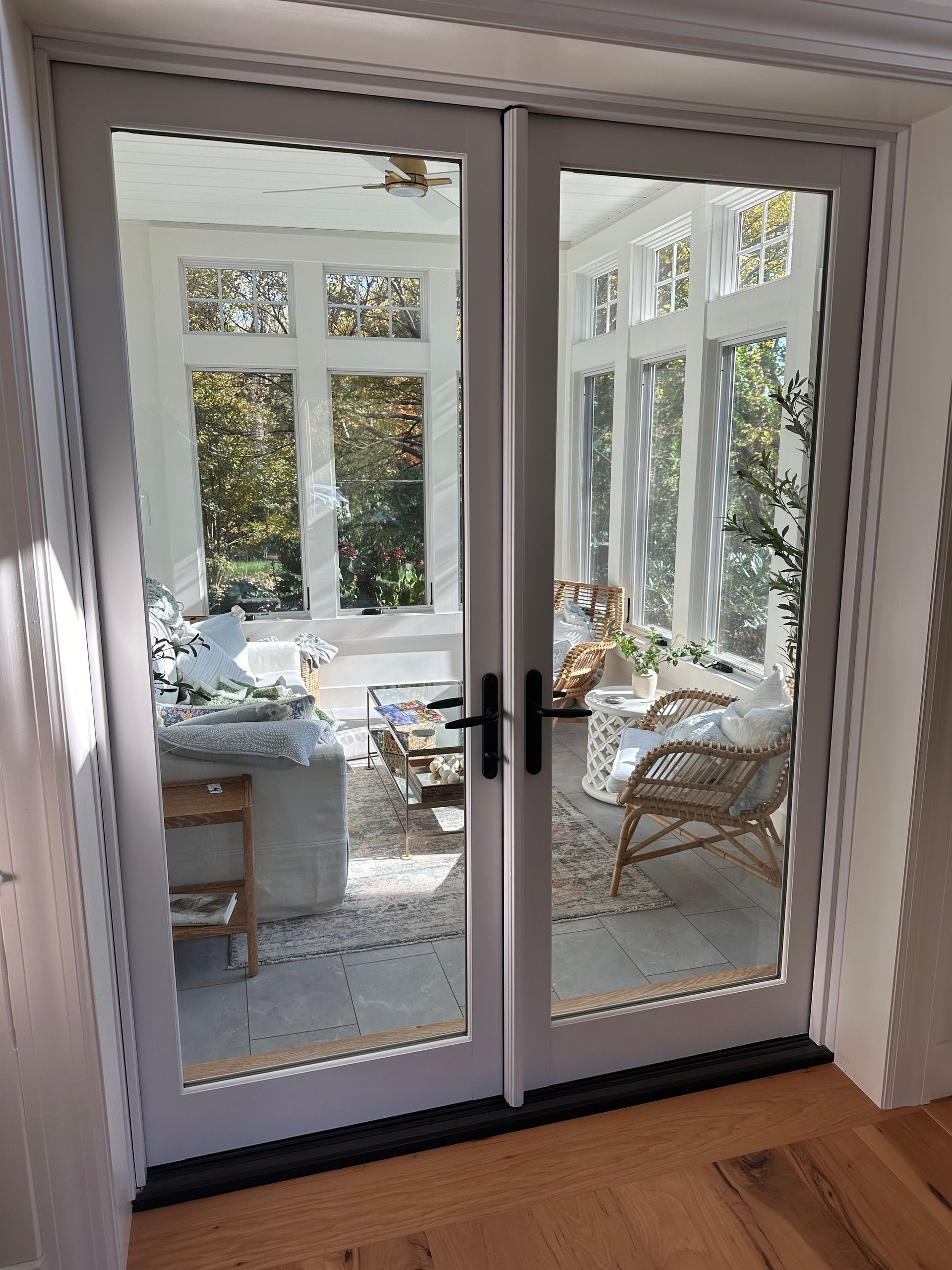 White French doors open to a sunroom with large windows, sunlight, and a seating area.