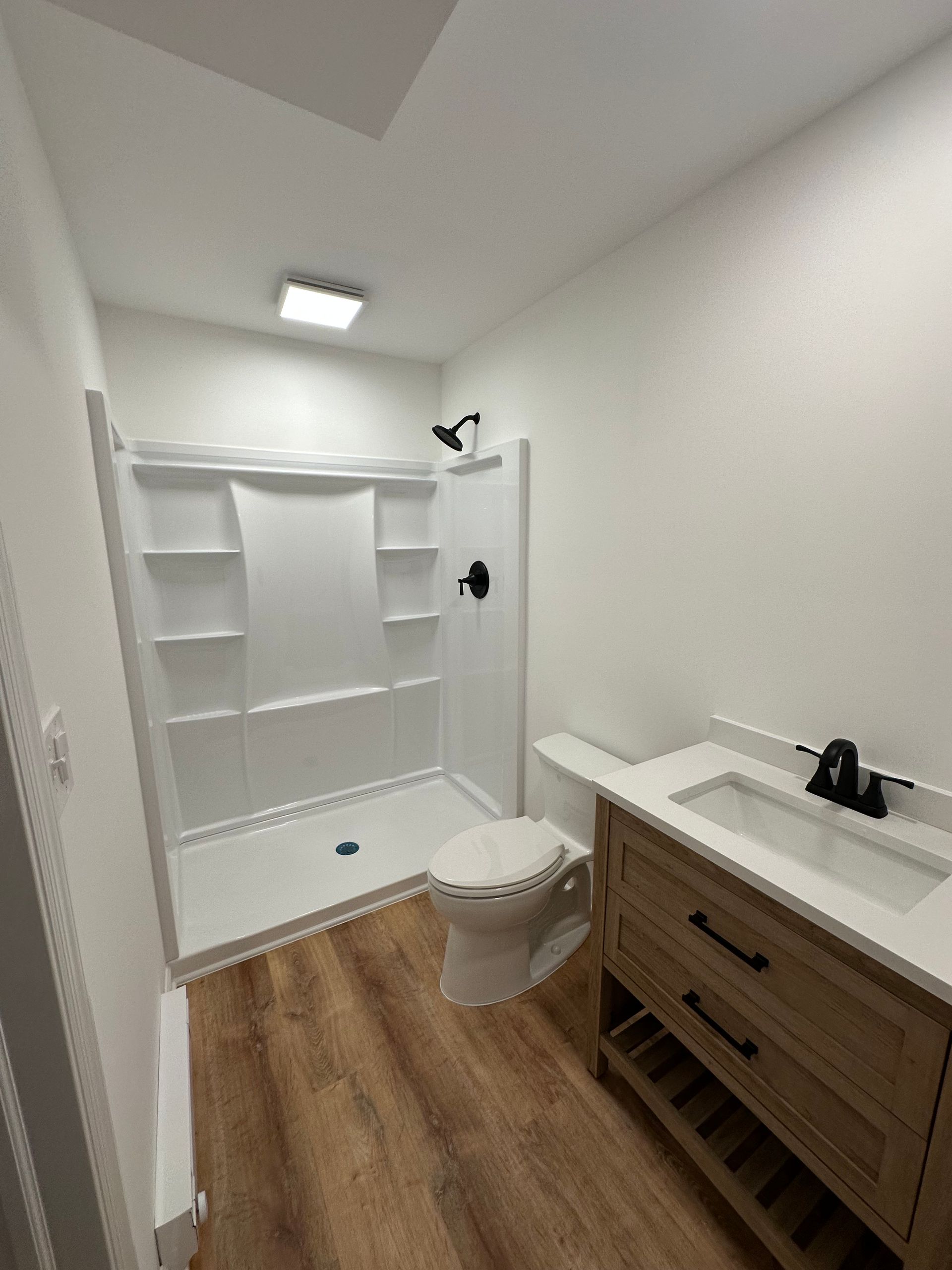Bathroom with a white shower, toilet, and vanity on a wood-look floor.