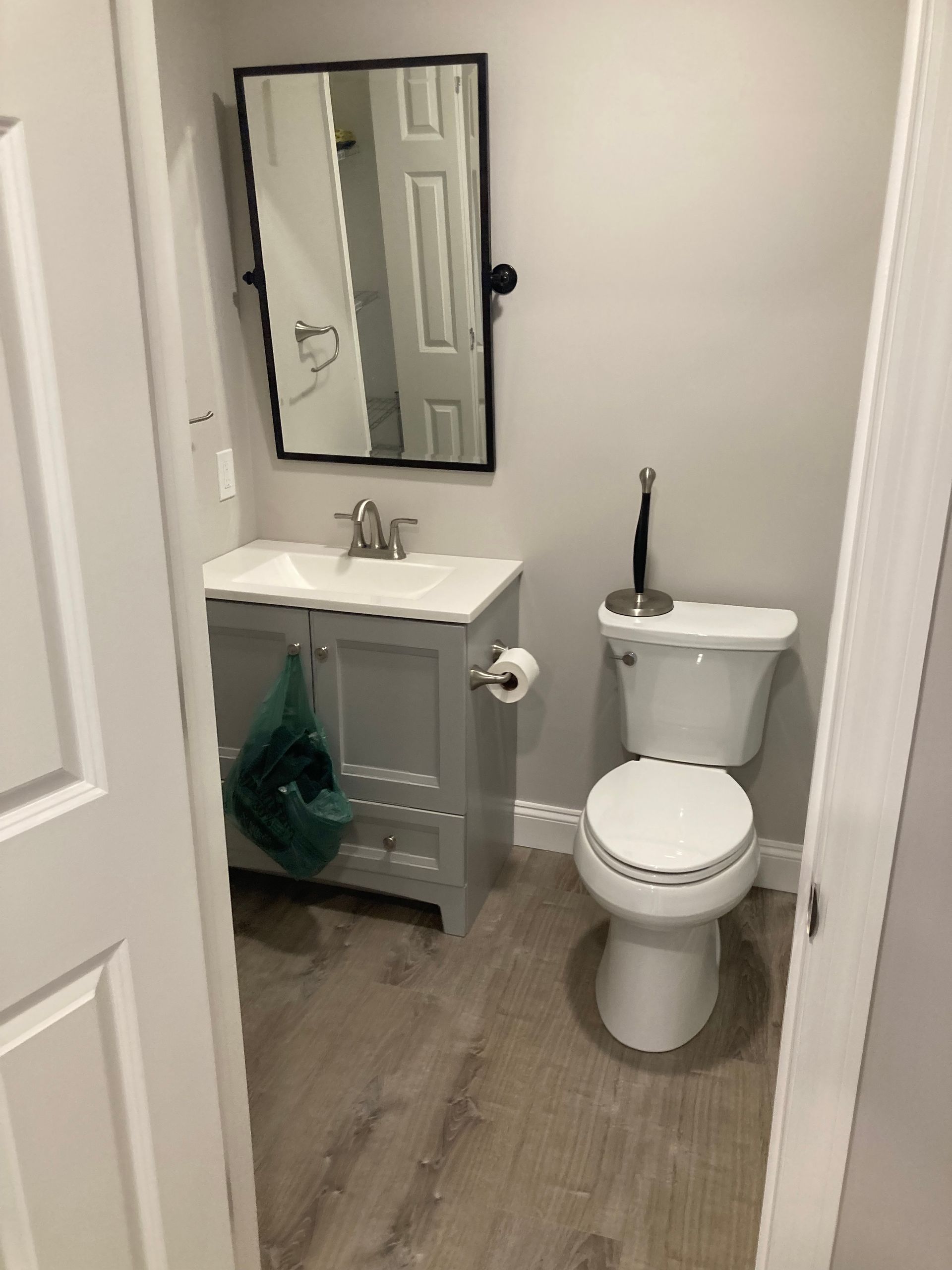 Small bathroom with gray vanity, toilet, mirror, and light gray walls.