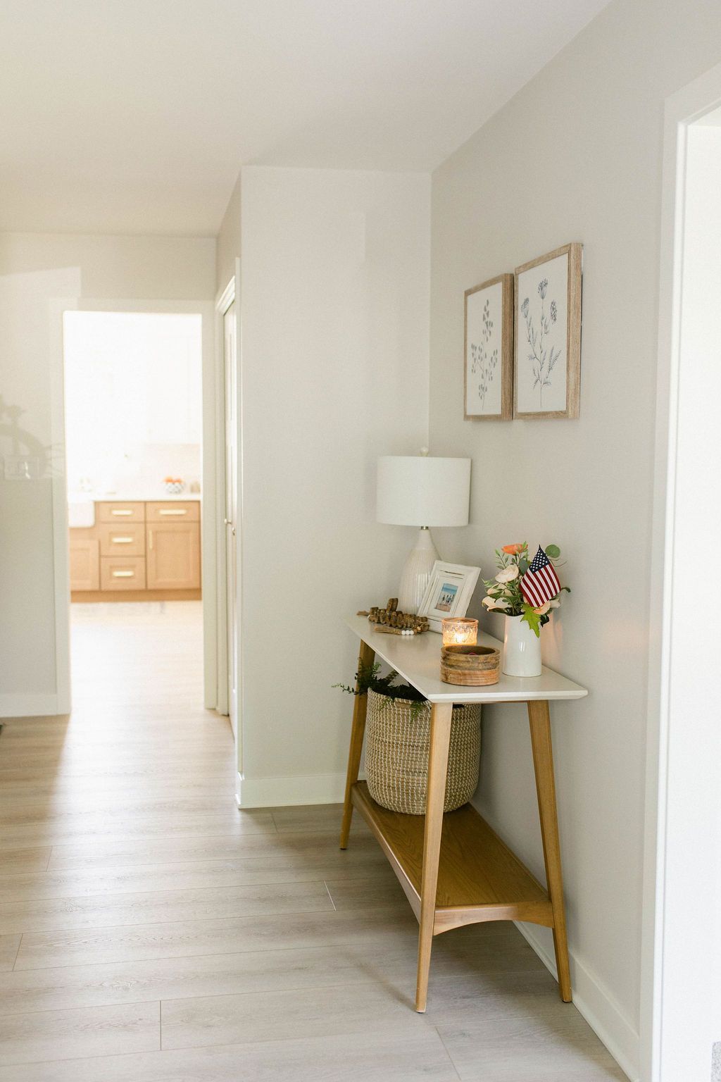 Hallway with light-colored walls, wood-tone console table holding decor, artwork, and lamp.