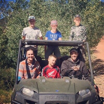 Family in an off-road vehicle in a sunny, outdoor setting. Smiling, posing near trees and red dirt.