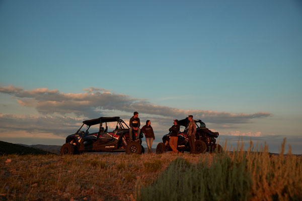 A group of people are standing next to four atvs in a field.