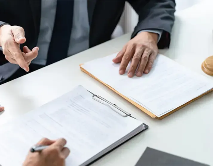 Two people in business attire review and sign professional documents at a desk.