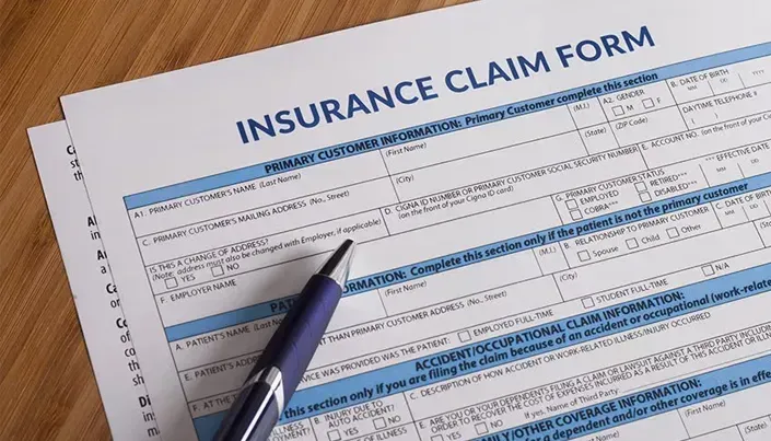 A blue pen resting on an insurance claim form on a wooden desk.