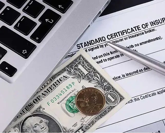 A laptop keyboard, a one-dollar bill with a coin on top, and a standard certificate of insurance on a surface.