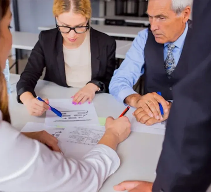 A diverse group of colleagues in business attire gather around a table, collaborating and reviewing documents together.