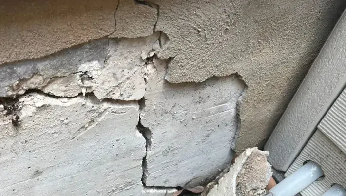 A close-up of a damaged exterior wall showing deep vertical cracks and crumbling concrete or stucco.