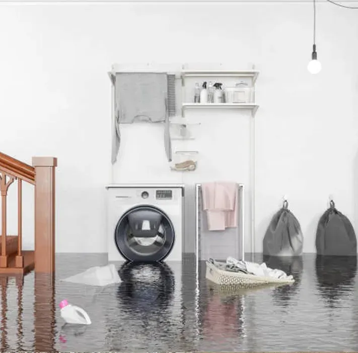 A laundry room flooded with water, with a washing machine, storage shelves, laundry baskets, and bags sitting in the pool.