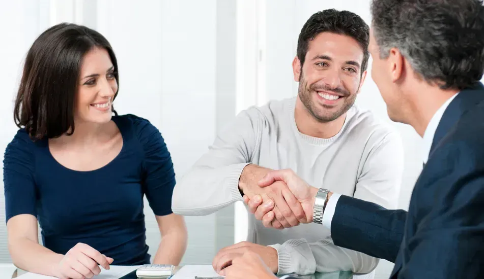 Two people smiling as they shake hands with a professional in an office setting.
