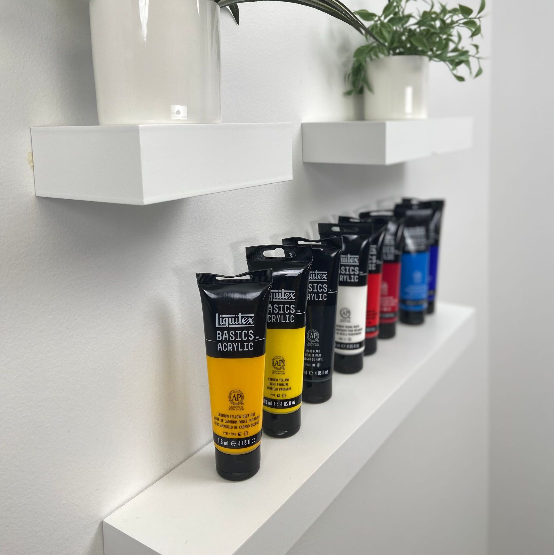 Assorted paint tubes in various colors arranged neatly on a white shelf.