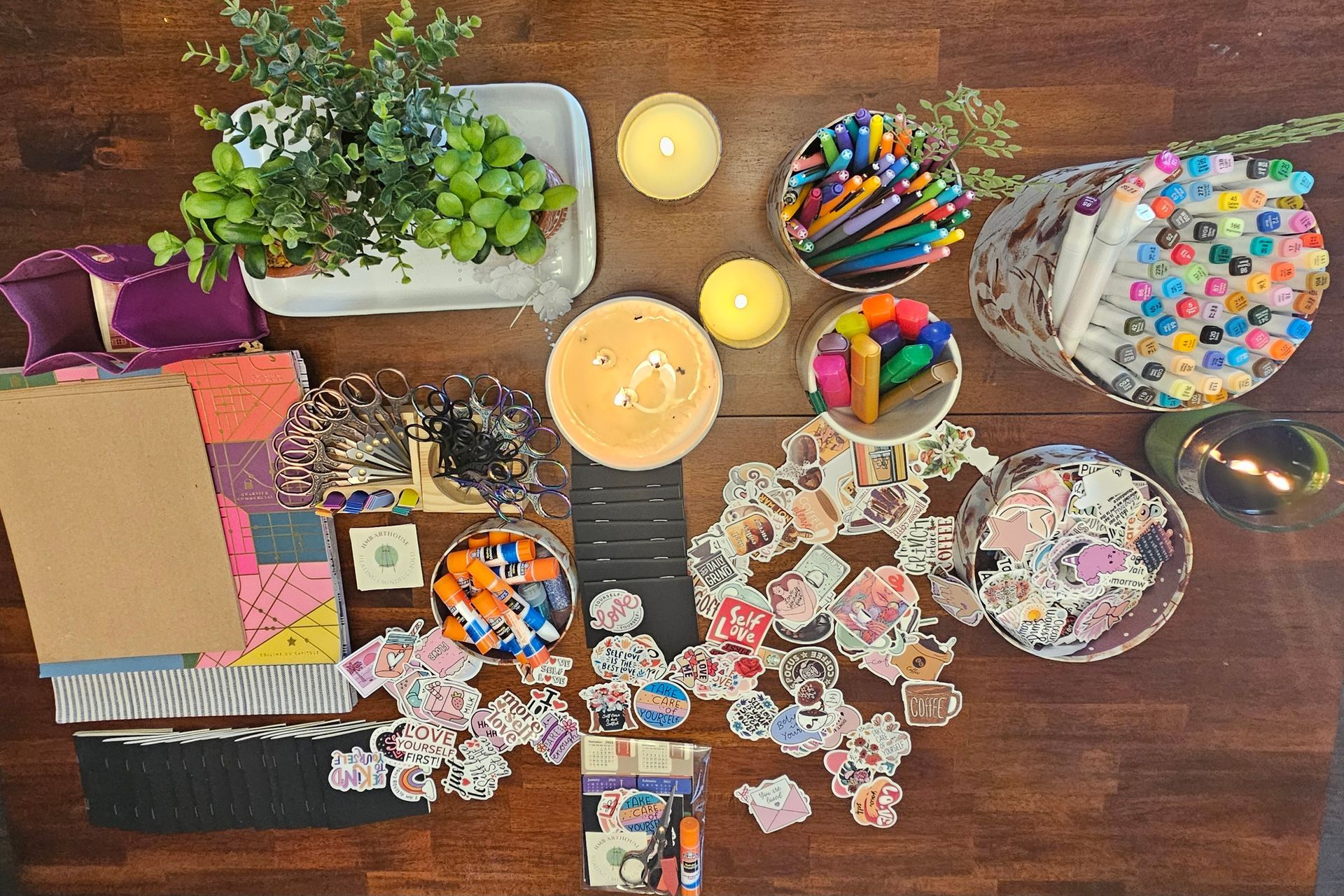 Assorted art supplies including glue sticks, stickers, markers, and paper scattered on a table for a creative project.