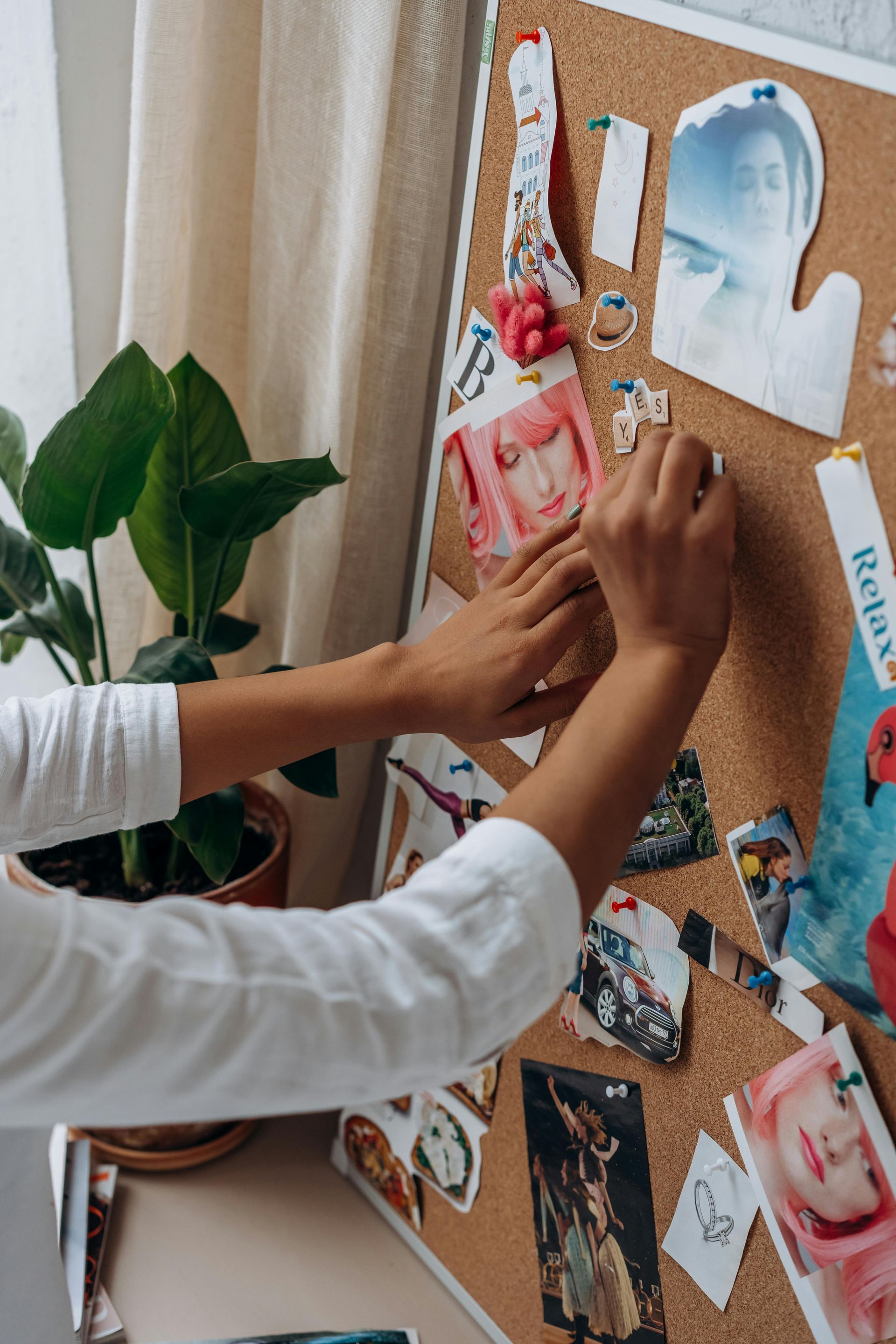 A woman attaching a photo to a mood board, surrounded by various images and design elements.