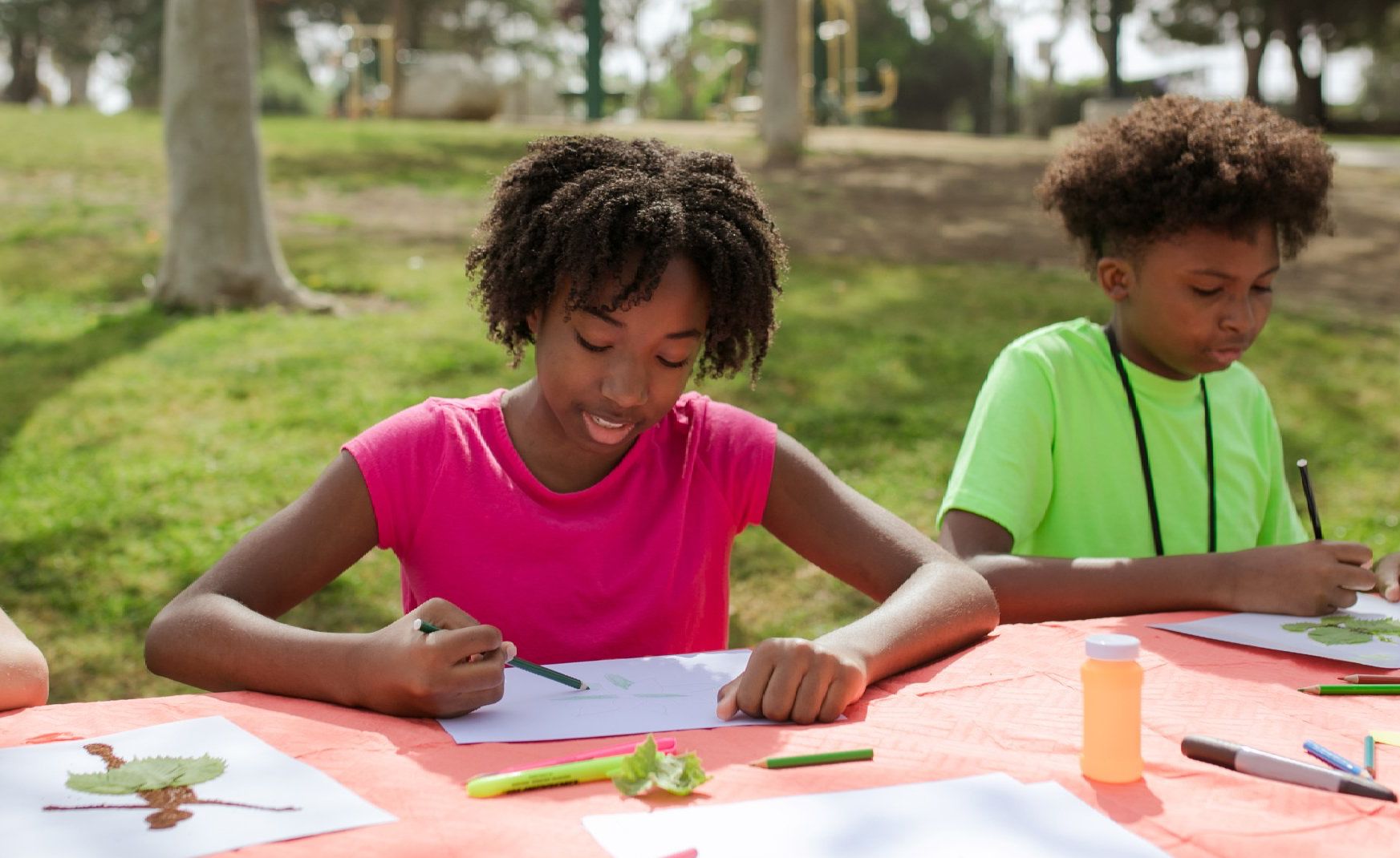 Children enjoying an outdoor art activity, drawing with colored pencils on a picnic table.