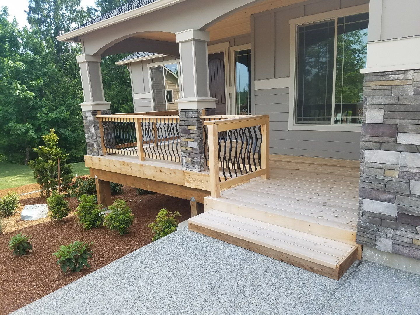 A porch with wooden deck and stairs. Decorative railings and stone accents. Gray siding.