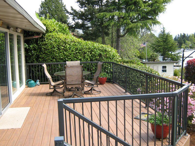 Wooden deck with metal railing and patio furniture overlooking trees and water.
