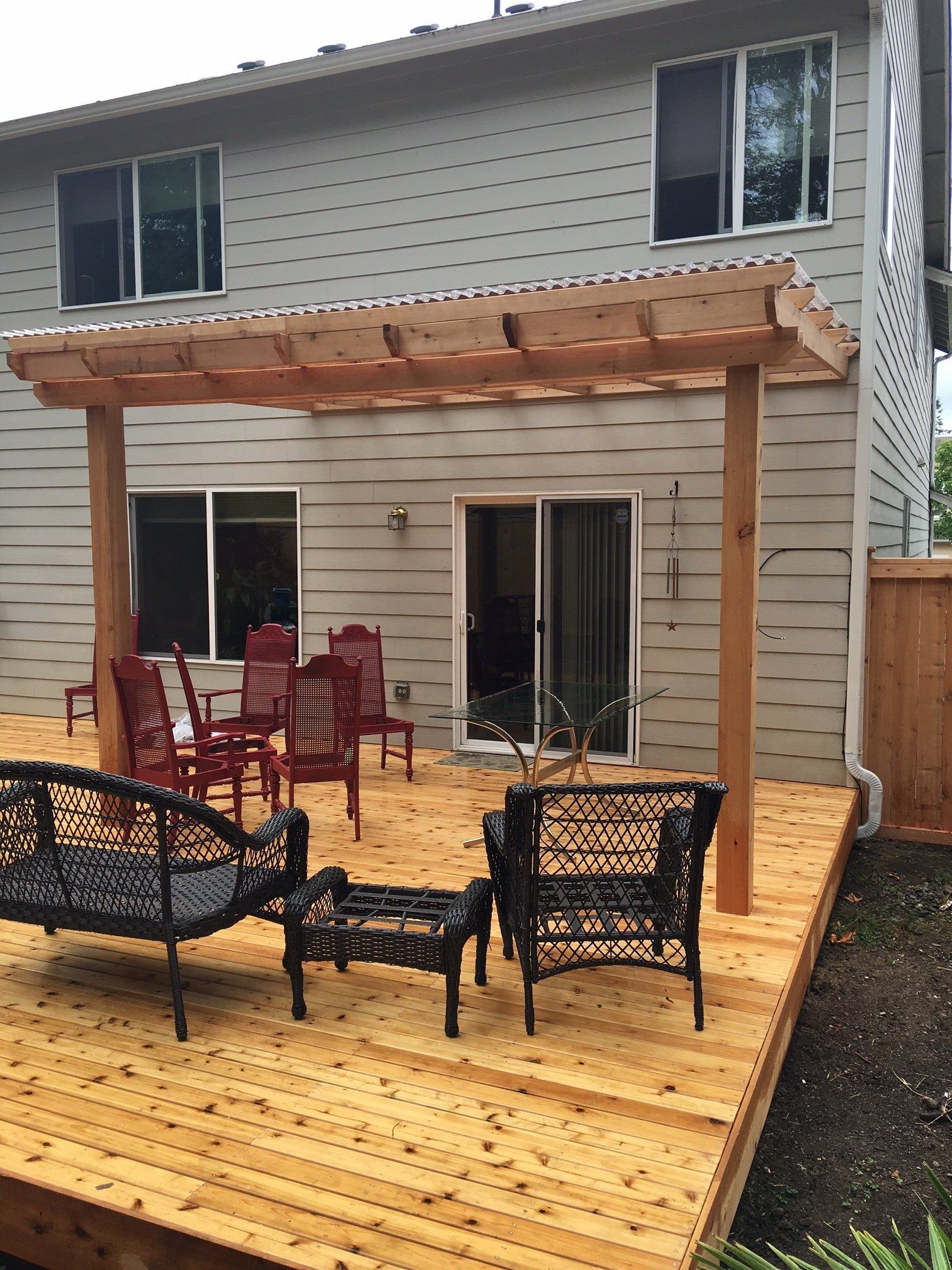 Wooden deck with patio furniture and pergola attached to a two-story house.