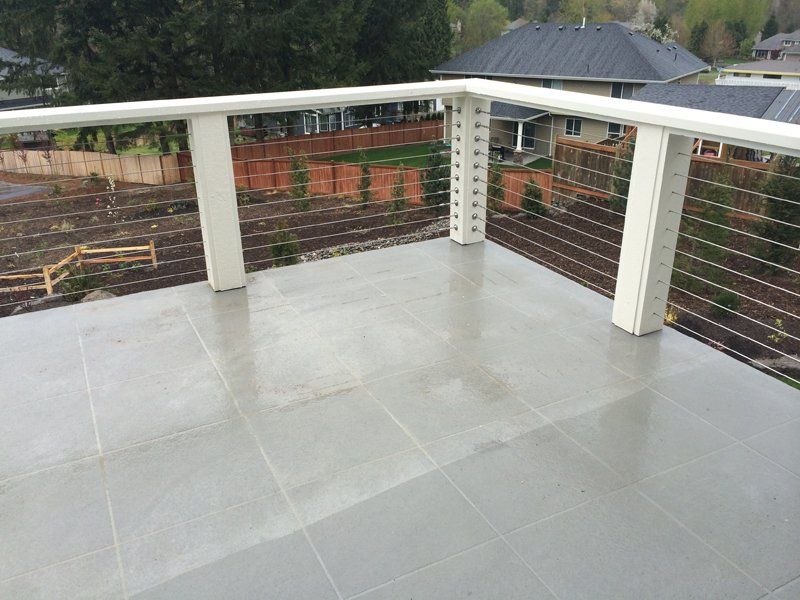 Gray tiled deck with white railing and cable balustrade overlooking a yard with a wooden fence.