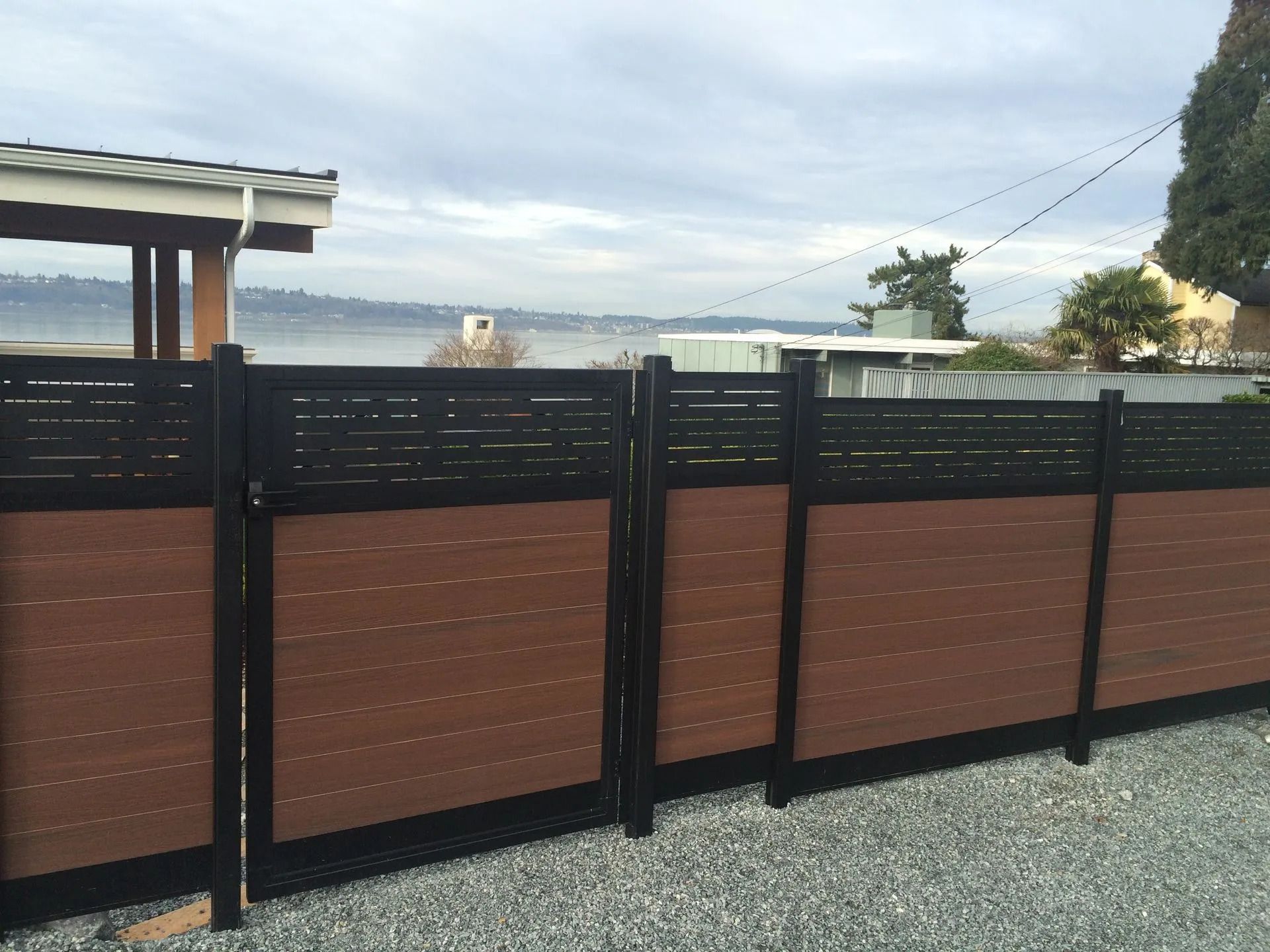 Brown and black horizontal slat fence with water and sky background.
