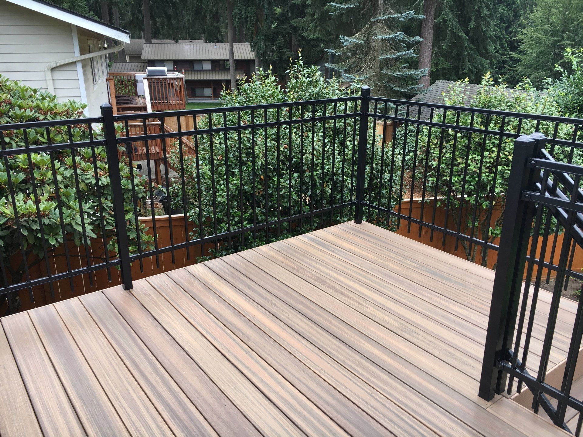 Wooden deck with black metal railing, surrounded by green shrubs.