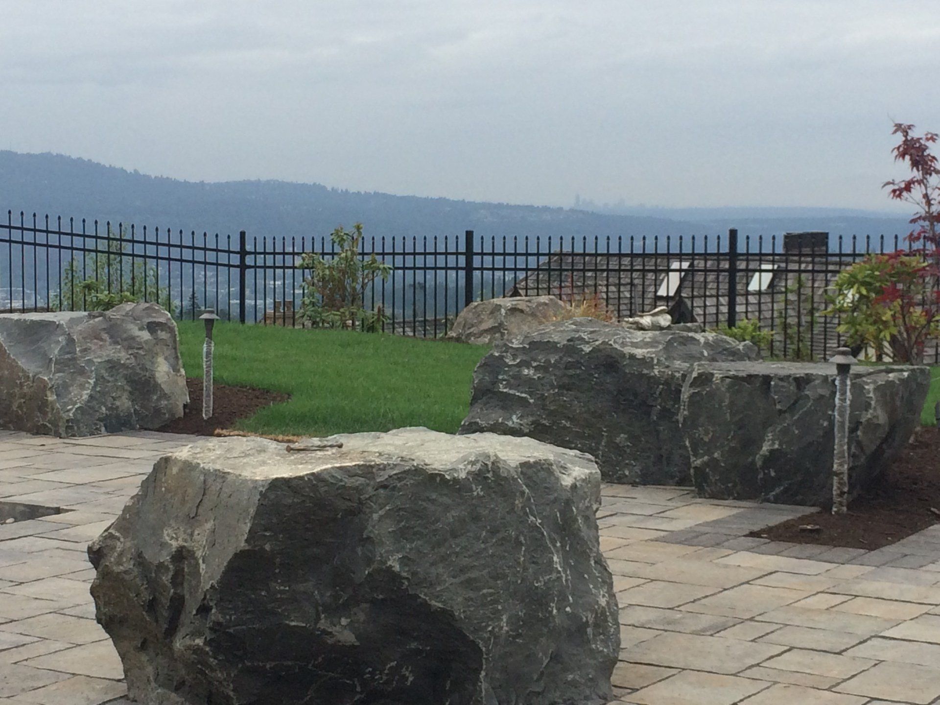 Large rock seating on patio overlooking a green lawn and distant mountains behind a black fence.