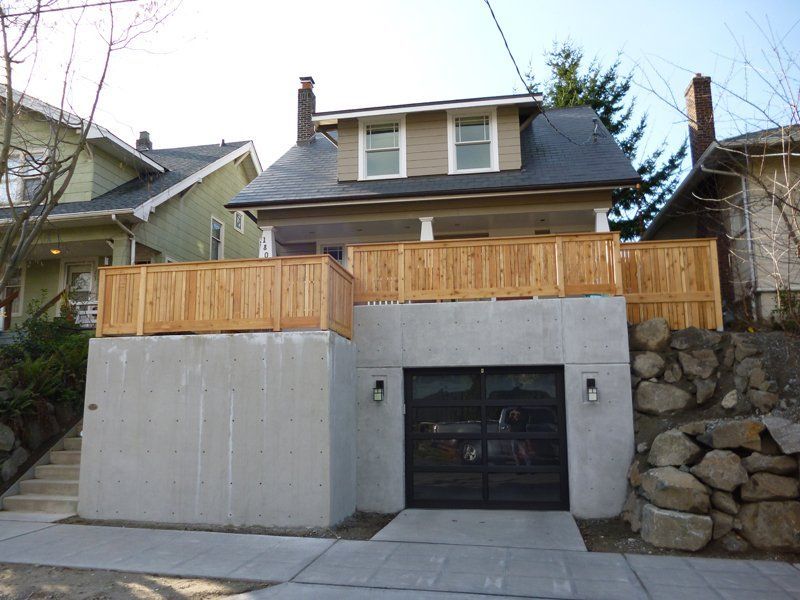 Beige house with a concrete garage, wooden deck, and a dark garage door.