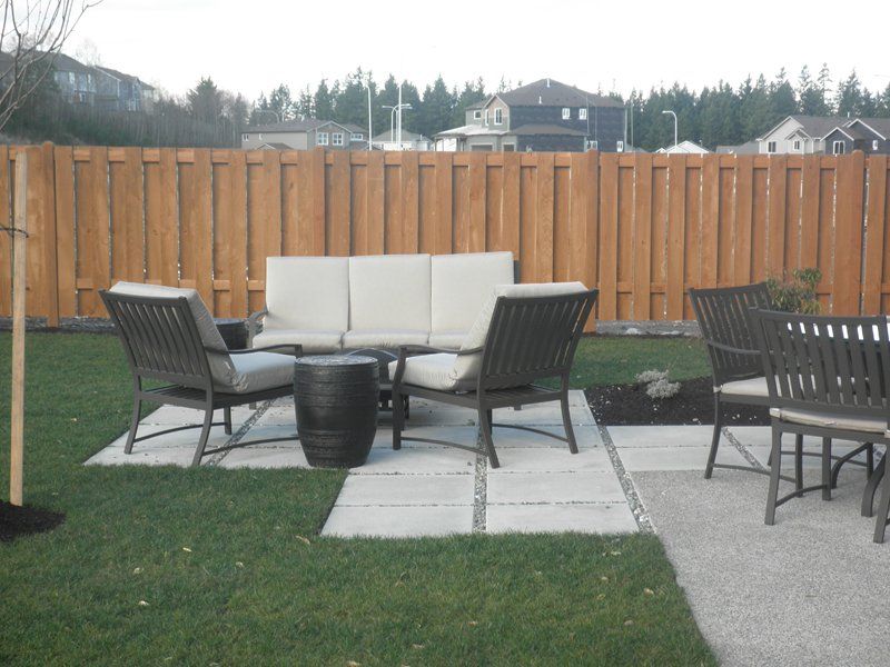 Outdoor seating area with sofa, chairs, and a table on patio slabs, in front of a wood fence.
