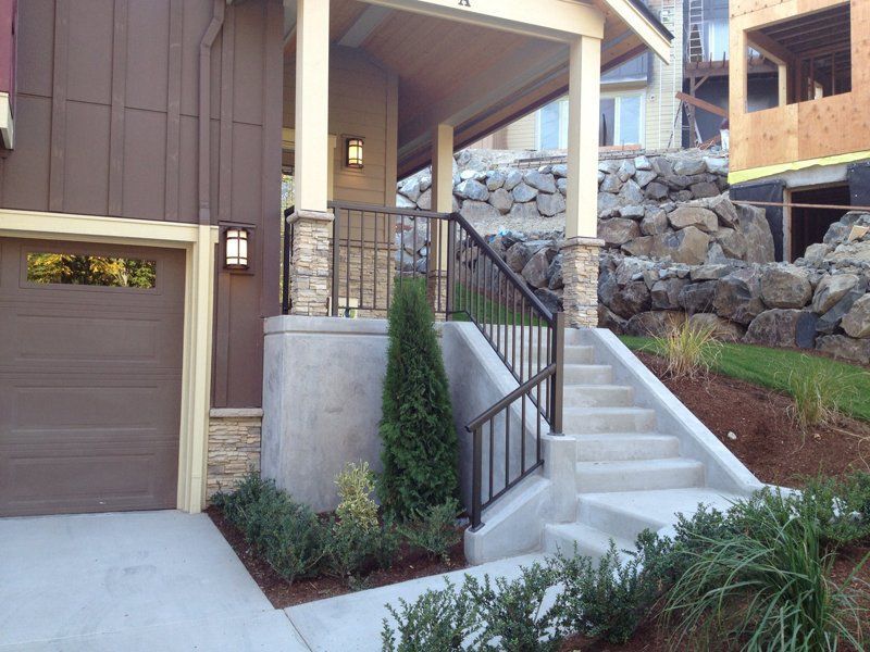 A house entrance with steps and a handrail leading to a covered porch and garage on the left.