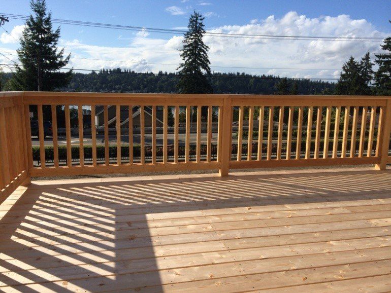 Wooden deck with light brown railing and vertical slats, casting shadows on the deck boards.