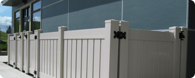 White picket fence in front of a building with dark windows. The fence has black hinges and is well lit.