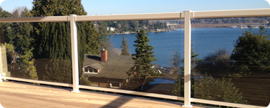 A glass railing overlooks a blue lake with houses and trees.