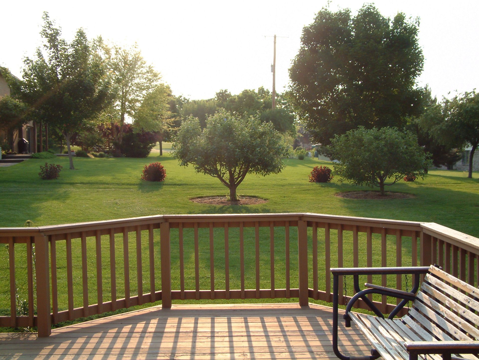 Wooden deck overlooking a grassy park with trees and a park bench.