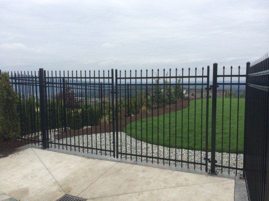Black metal fence with pointed tops encloses a green lawn, view of hills in the background.