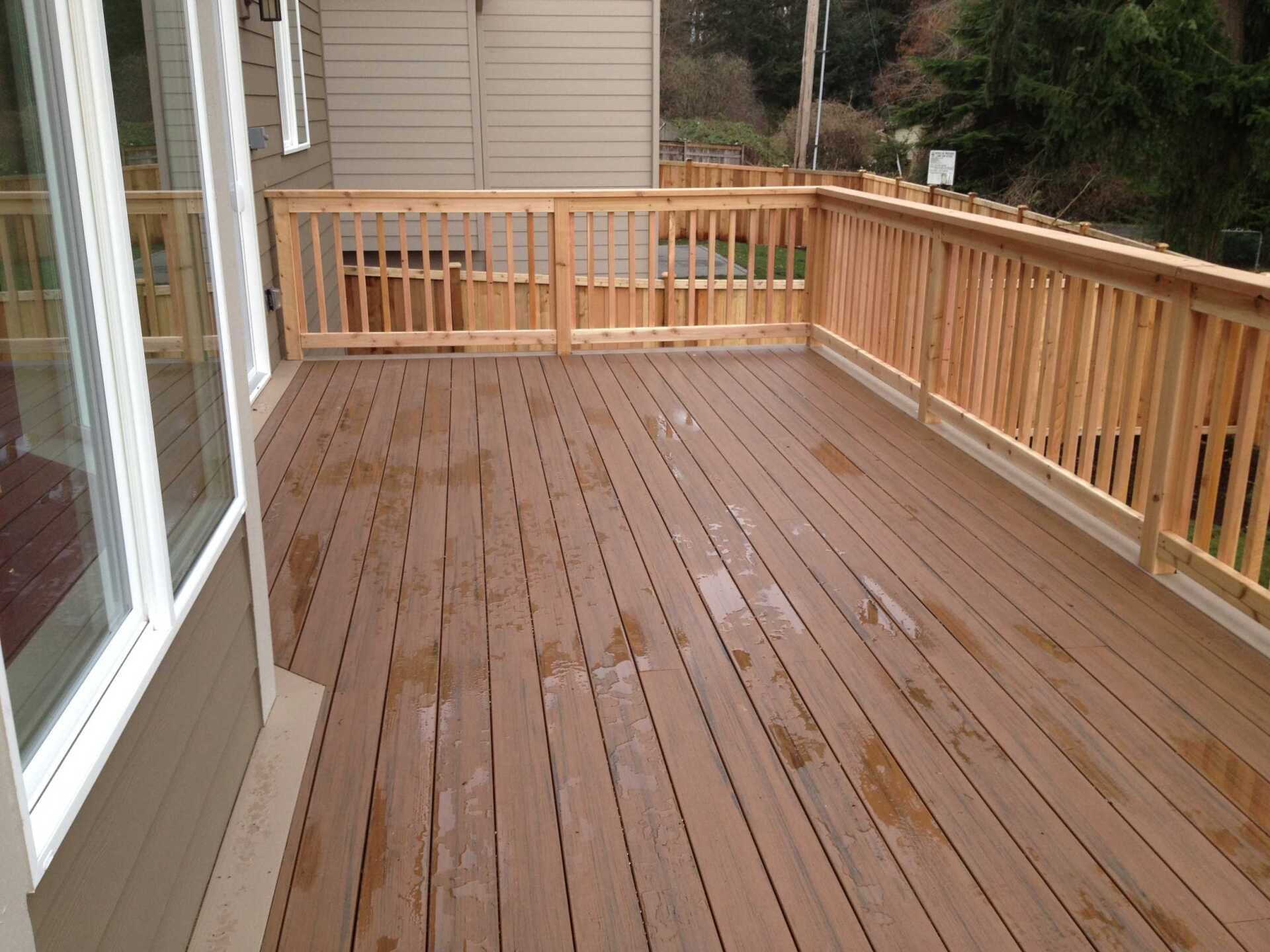 Wooden deck with light brown planks and railing, attached to a light-colored house.