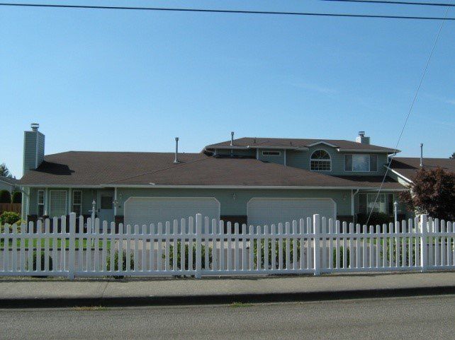 A two-story light green house with a white picket fence under a blue sky.