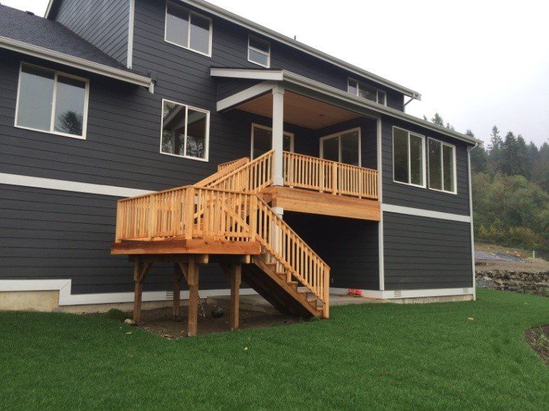 Wooden deck attached to a dark-sided house with stairs leading to a covered area and the lawn.
