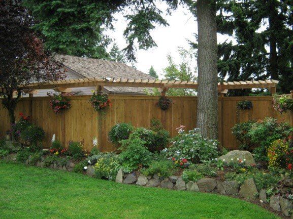 Wooden fence with a pergola, flower boxes, and a garden in front.