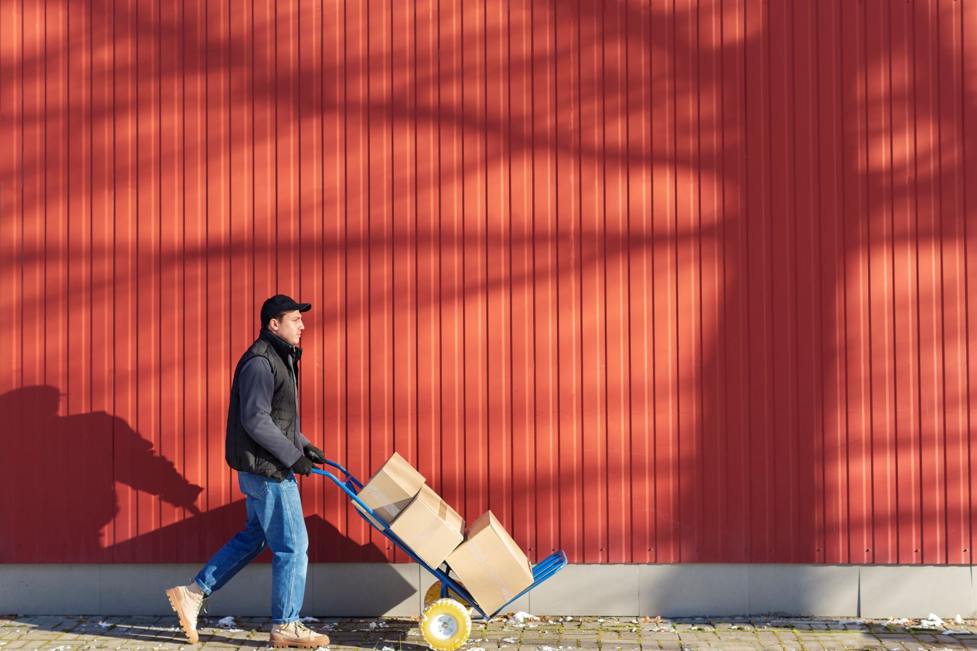 A man is pushing a cart with boxes on it in front of a red wall.