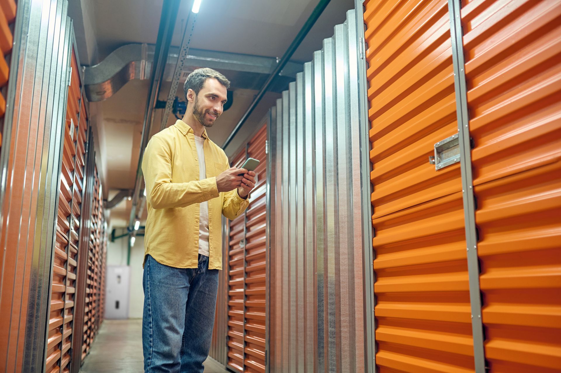 A man is standing in a storage room looking at his cell phone.