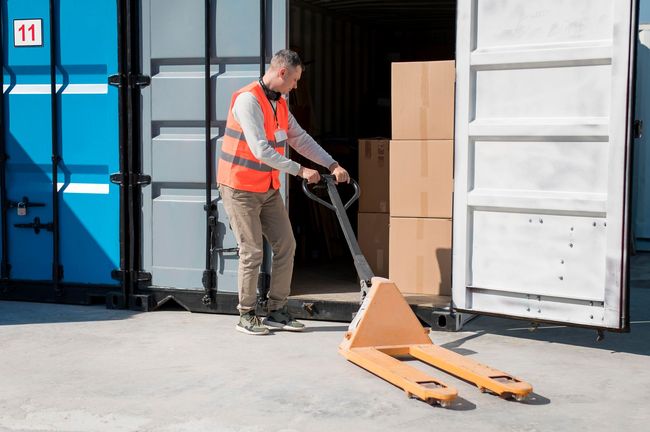 A man is pushing a pallet truck into a shipping container.